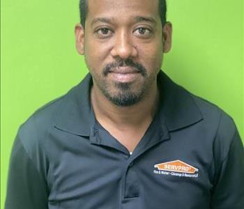 Male Employee with black shirt, smiling with green wall background.